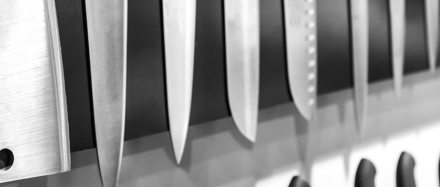 A chef in a white jacked holds a knife and a knife sharpener